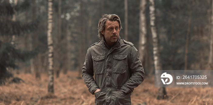 Blonde rugged man in green coat in woodland.