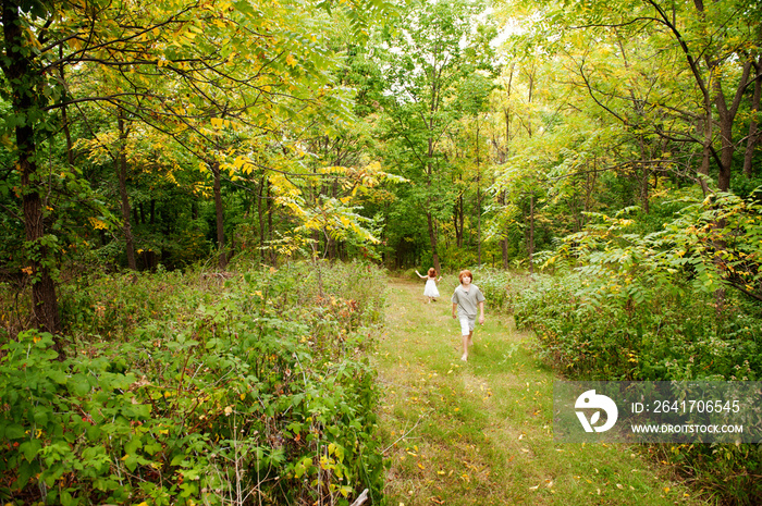 Brother (12-13) and sister (6-7) walking on path through woods