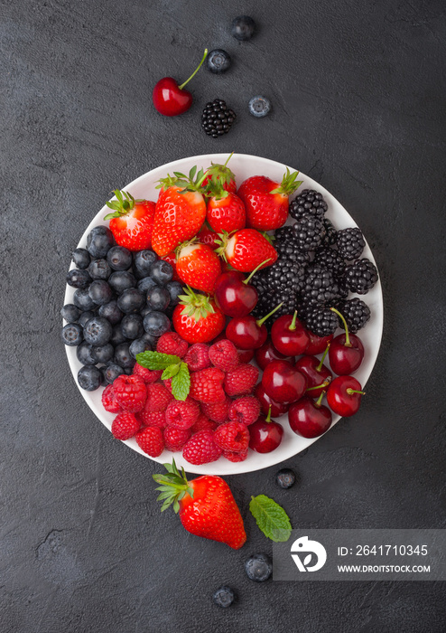 Fresh organic summer berries mix in white plate on black kitchen table background. Raspberries, stra