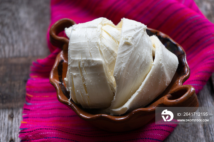 Fresh Oaxaca cheese in clay pot on wood background