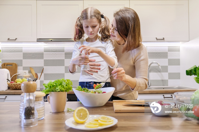 Cooking healthy home meal by family. Woman teaching and helping the girl to salt and pepper a fresh 