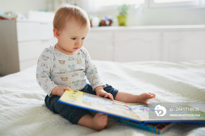 Baby girl sitting on bed and reading a book