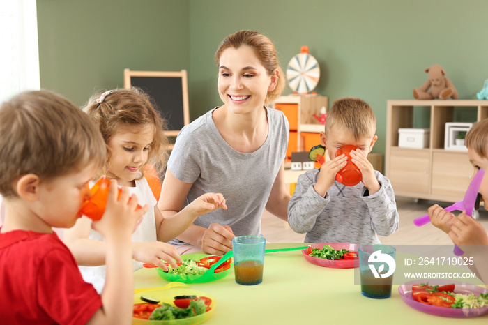 Nursery teacher with cute little children during lunch in kindergarten