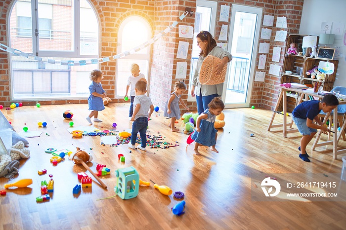 Beautiful teacher and group of toddlers playing around lots of toys at kindergarten