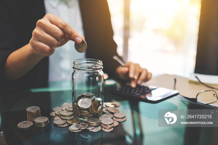 Closeup image of a businesswoman stacking and putting coins in a glass jar