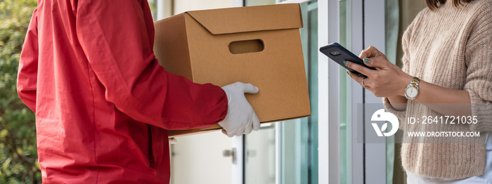 一名身穿红色制服的亚裔送货员在房前将包裹递给一名女性顾客。一个pos