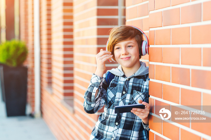 Pre-teenage boy with headphones and mobile phone listening to music at city street. Fashion boy hair