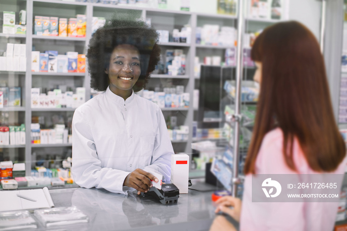 Caucasian woman customer making payment in drugstore. African woman pharmacist dispensing drug, hold