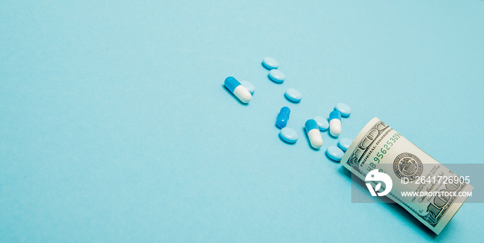 Money rolled up with pills flowing out isolated on blue background, high costs of expensive medicati