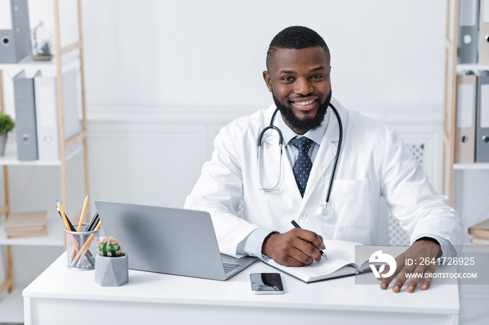 Smiling black doctor working with laptop in office