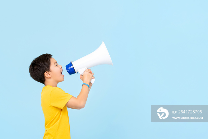 Cute 10 year old  boy shouting on megaphone isolated on light blue background with copy space