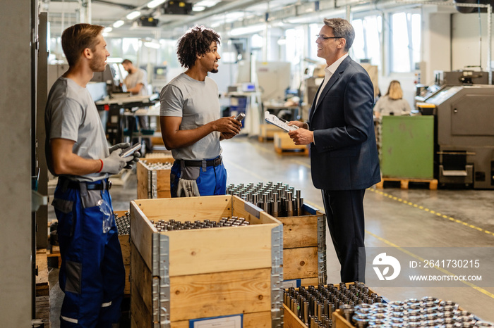 Happy businessman talking with metal workers while visiting the production facility.