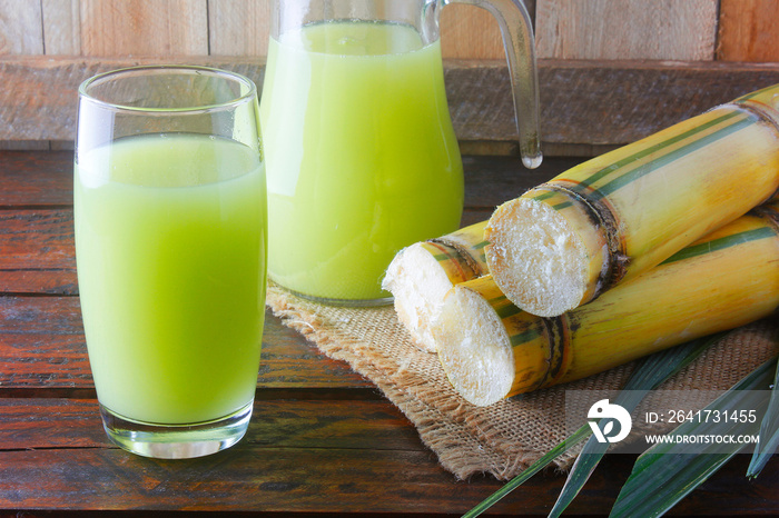 Fresh sugar cane juice in a jar with cut pieces of cane on rustic wooden table