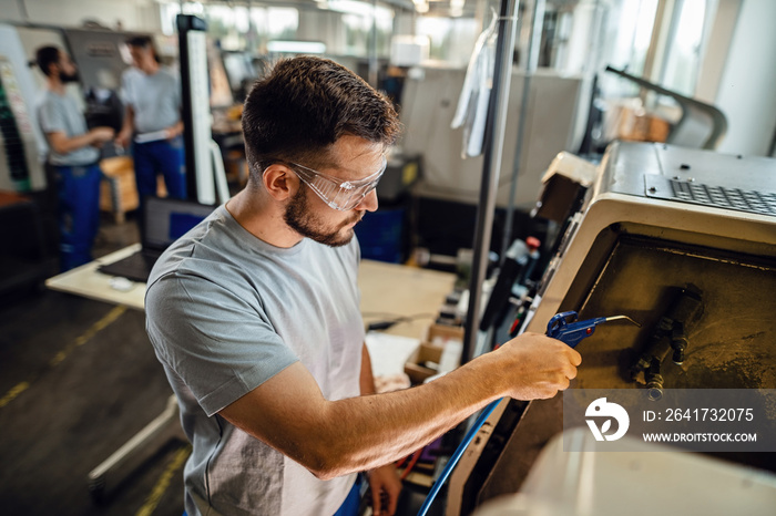 Young industrial engineer operating a CNC machine at production line.