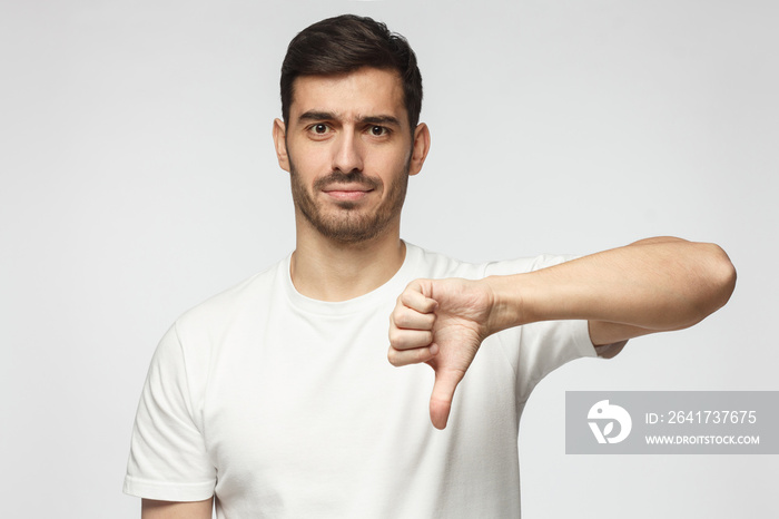 Young man showing thumb down or dislike, isolated on gray background