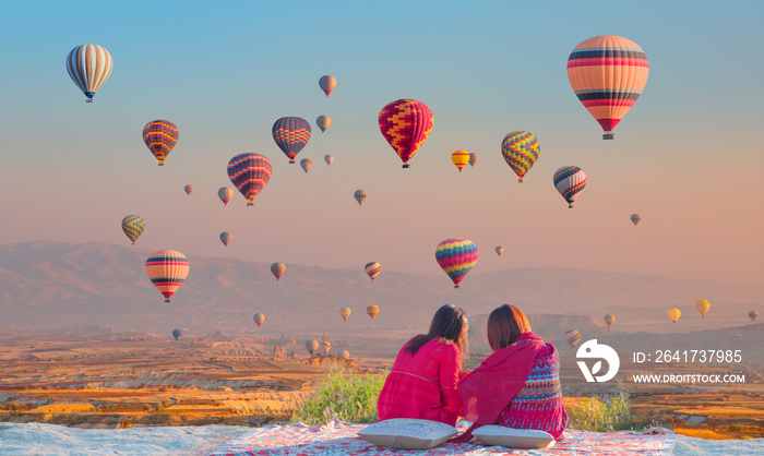 Hot air balloon flying over spectacular Cappadocia - Girls watching hot air balloon at the hill of C