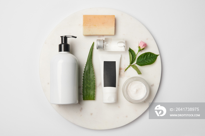 Top view of different cosmetic containers, soap, aloe vera leaf and rose flower on white round surfa