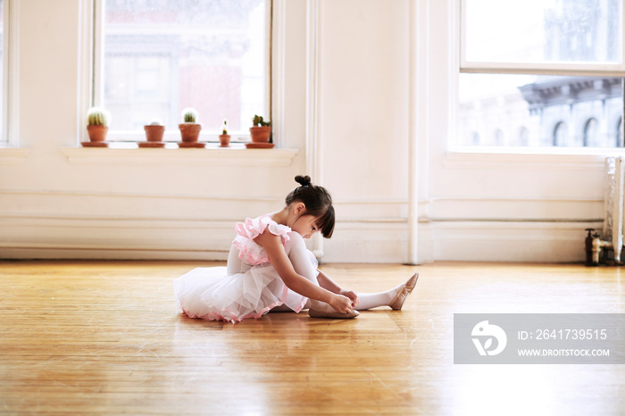 Side view of ballerina tying ballet shoe in studio