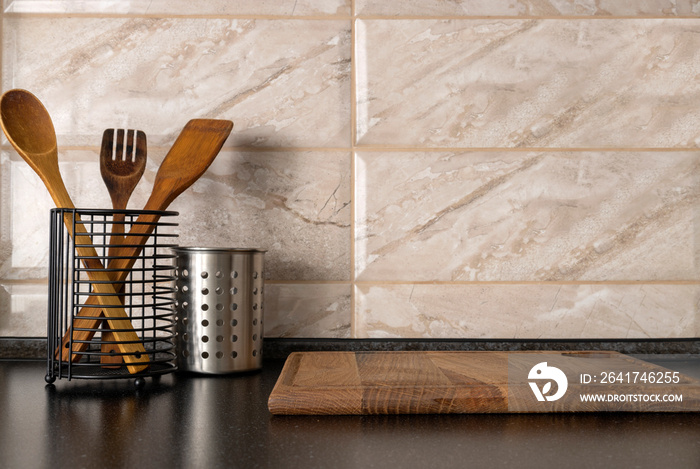 Closeup of metallic cups for storage kitchen utensils,wooden board on the black table against brown 