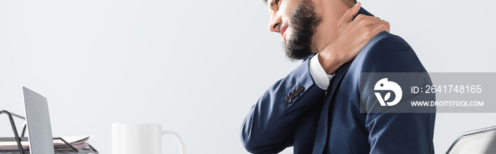 Businessman suffering from neck pain near laptop and cup on blurred foreground, banner