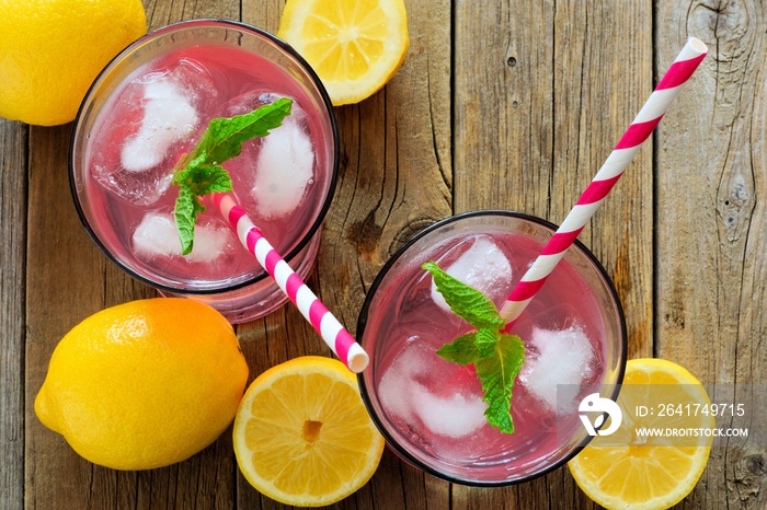 Two glasses of lemonade with straws and mint, overhead view on rustic wooden background