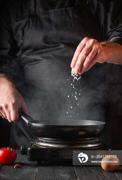 The chef adds salt while cooking eggs in pan. Work environment on vintage kitchen table. Vertical im