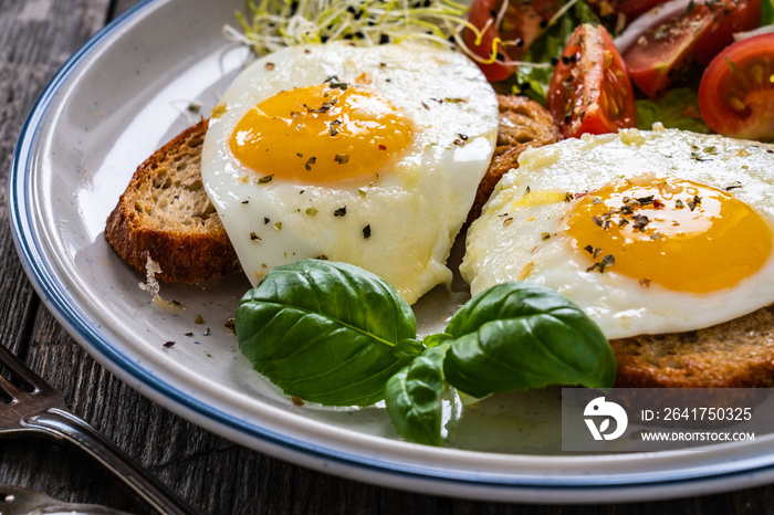 Sunny side up eggs on toasted bread, parmesan and fresh vegetables on wooden table