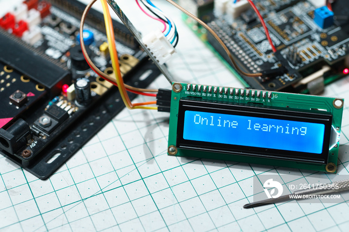 Closeup, Blue LCD display screen showing  Online Learning  word, wire connected with computer board 