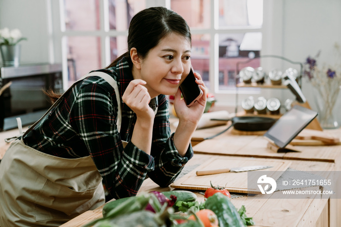 年轻快乐的亚裔日本女人穿着围裙在手机上与数字表格中的在线食谱交谈