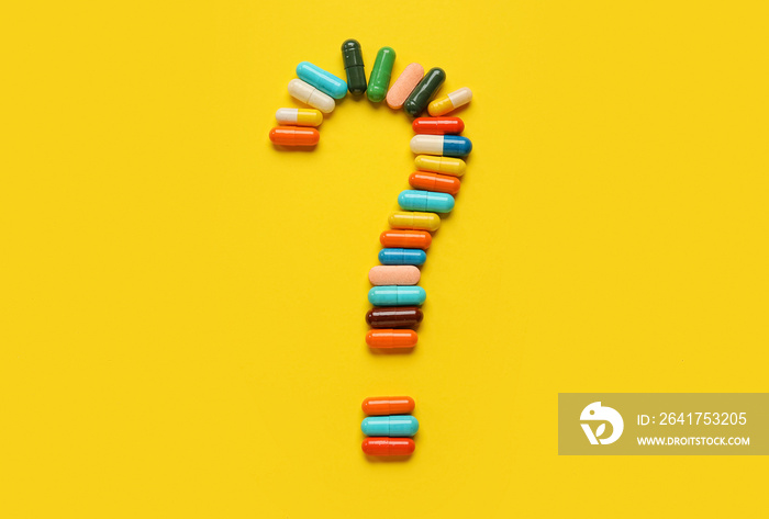 Question mark made of capsules on yellow background