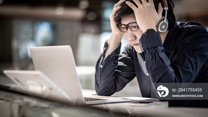 Overworked Asian businessman feeling stressed and headache while working with laptop computer at hom