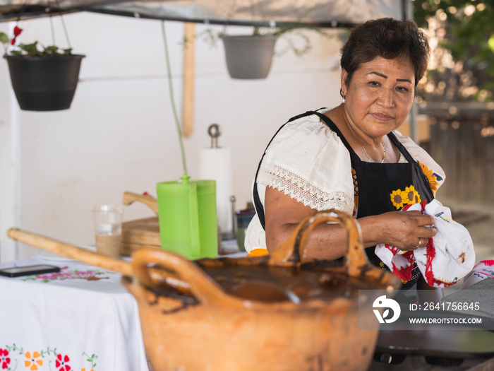 Horizontal image of an Indigenous woman looking at a clay pot with mole