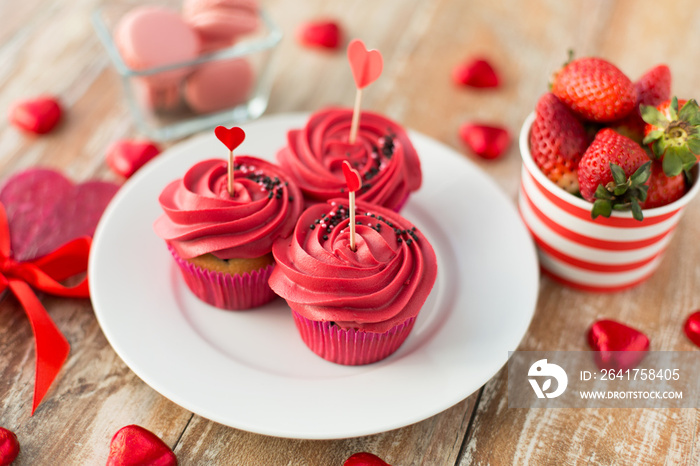 valentines day and sweets concept - close up of frosted cupcakes, red heart shaped chocolate candies