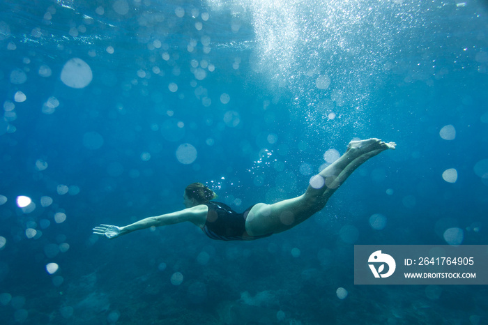 underwater photo of young woman in swimming suit diving in ocean alone