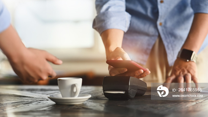 Cropped image of man using a smartphone for making a bill payment at credit card reader with the caf