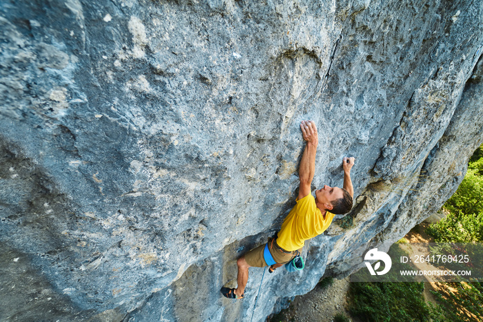 top view of man rock climber in yellow t-shirt, climbing on a cliff, searching, reaching and grippin