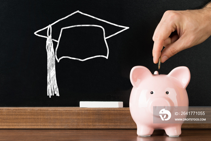 Person Inserting Coin In Piggybank For Completing Education