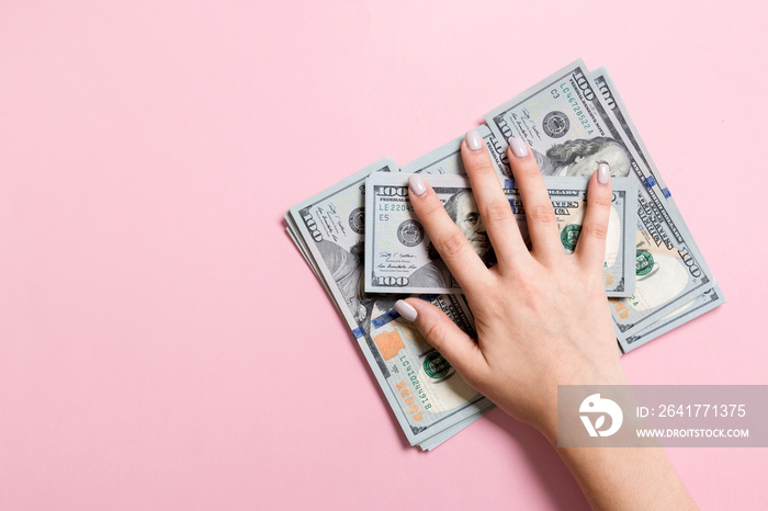 女性双手躺在一堆100美元钞票上的俯视图。成功与财富概念