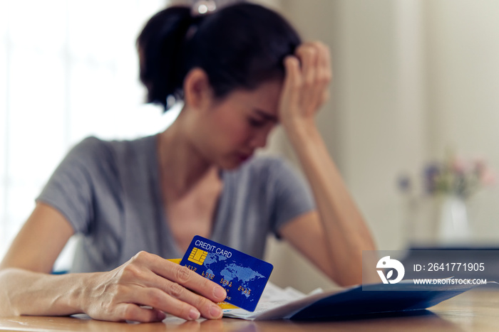 压力重重的年轻亚洲女性坐着，手里拿着信用卡和账单，担心找不到钱支付