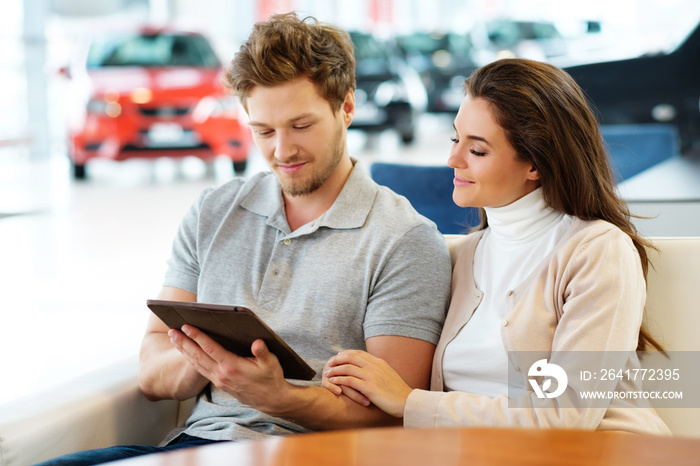 Beautiful young couple looking a new car at the dealership showroom