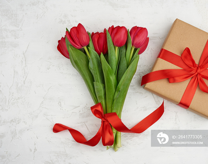 bouquet of red blooming tulips with green leaves, wrapped gift in brown craft paper