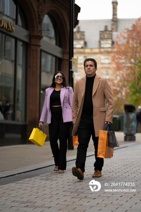 Father and adult daughter carrying shopping bags in street