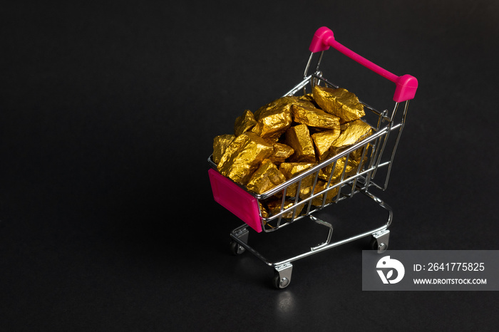 A pile of gold nuggets or gold ore in shopping cart or supermarket trolley on black background, prec