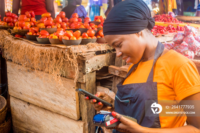 young african woman selling in a local african market holding a mobile point of sale system and usin