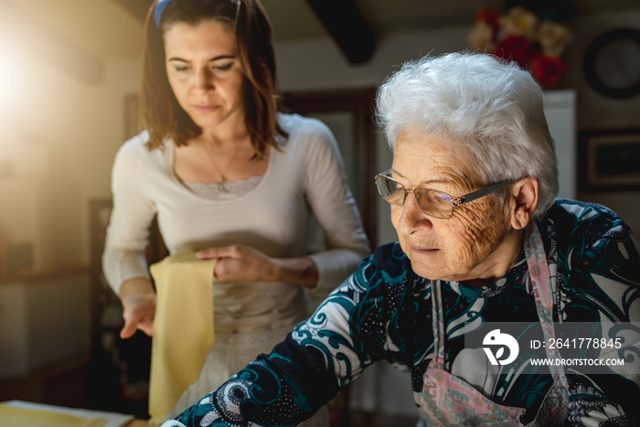 Caucasian grandmother teaching to granddaughter how to prepare fresh homemade pasta. Spending time i