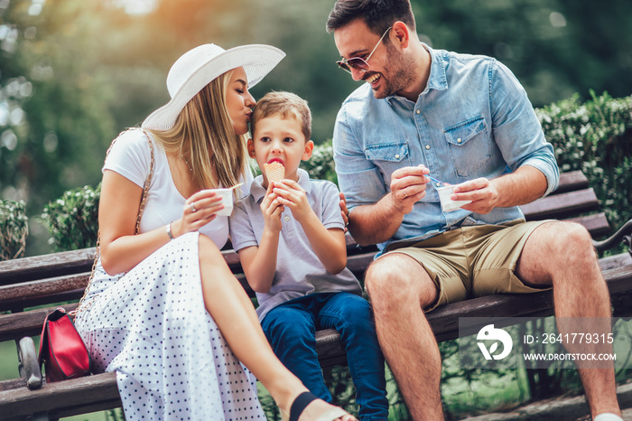 Young happy family spending their weekend in the park. They are eating the ice cream.