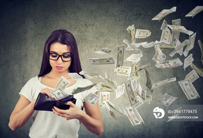 Sad woman looking at her wallet with money dollar banknotes flying out away