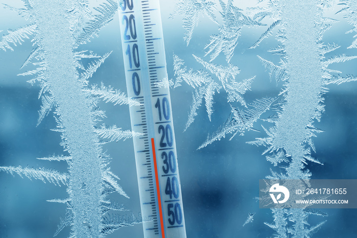 Frosty winter window with ice patterns and a thermometer showing a minus temperature