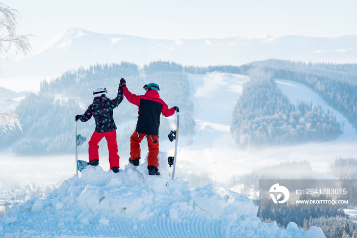 一对情侣在雪山顶上击掌合影，观察令人惊叹的冬天