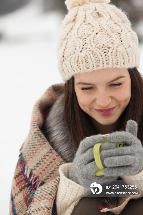 Smiling young woman in warm clothing enjoying hot coffee